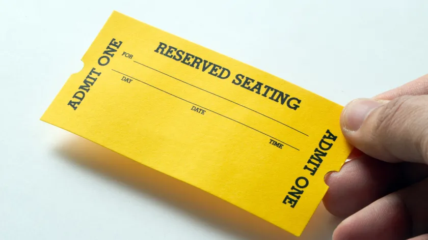 Hand holding a yellow reserved seating ticket with admit one text on a white background.